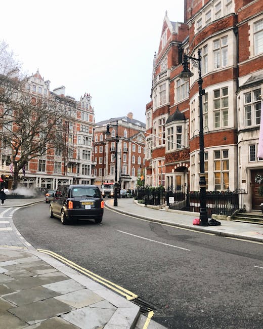A street scene on Brompton Road featuring residential buildings with red brick facades, white window frames, and decorative architectural elements. The street is lined with black wrought iron fencing 